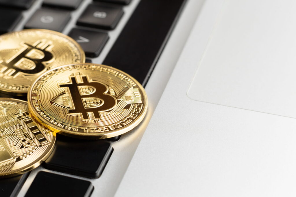 Zu sehen ist ein Laptop im Hintergrund auf dem Münzen (Bitcoins) liegen. Diese Abbildung soll Kryptowährung visualisieren.